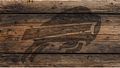 A rustic dark brown wood plank surface with a large black engraved or burned graphic of a bird, likely a hawk or eagle, across the center.