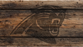 A dark brown graphic of a roaring animal head, resembling a wolf or wild cat, overlaid on a rustic horizontal wooden plank background.